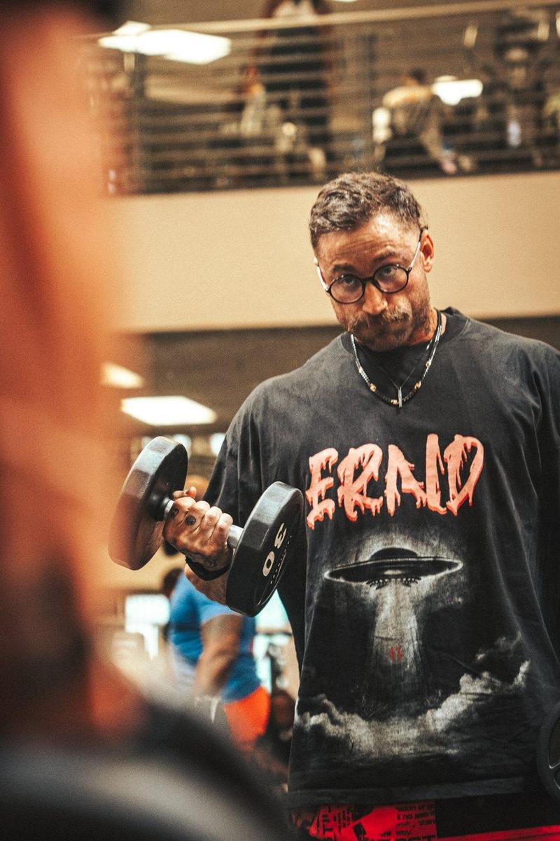 Athlete in round glasses curling a dumbbell in an ERND graphic tee