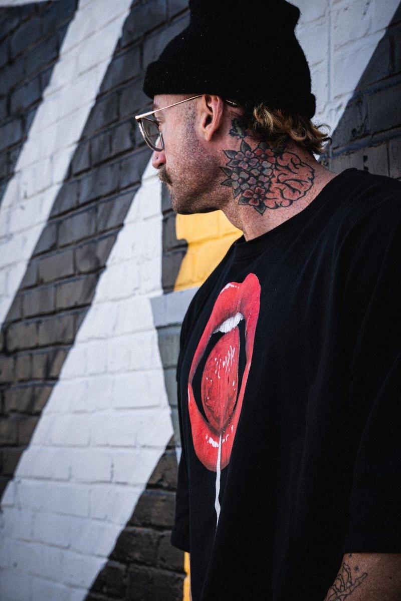 Tattooed athlete in a beanie in profile against a striped mural, red lips graphic tee