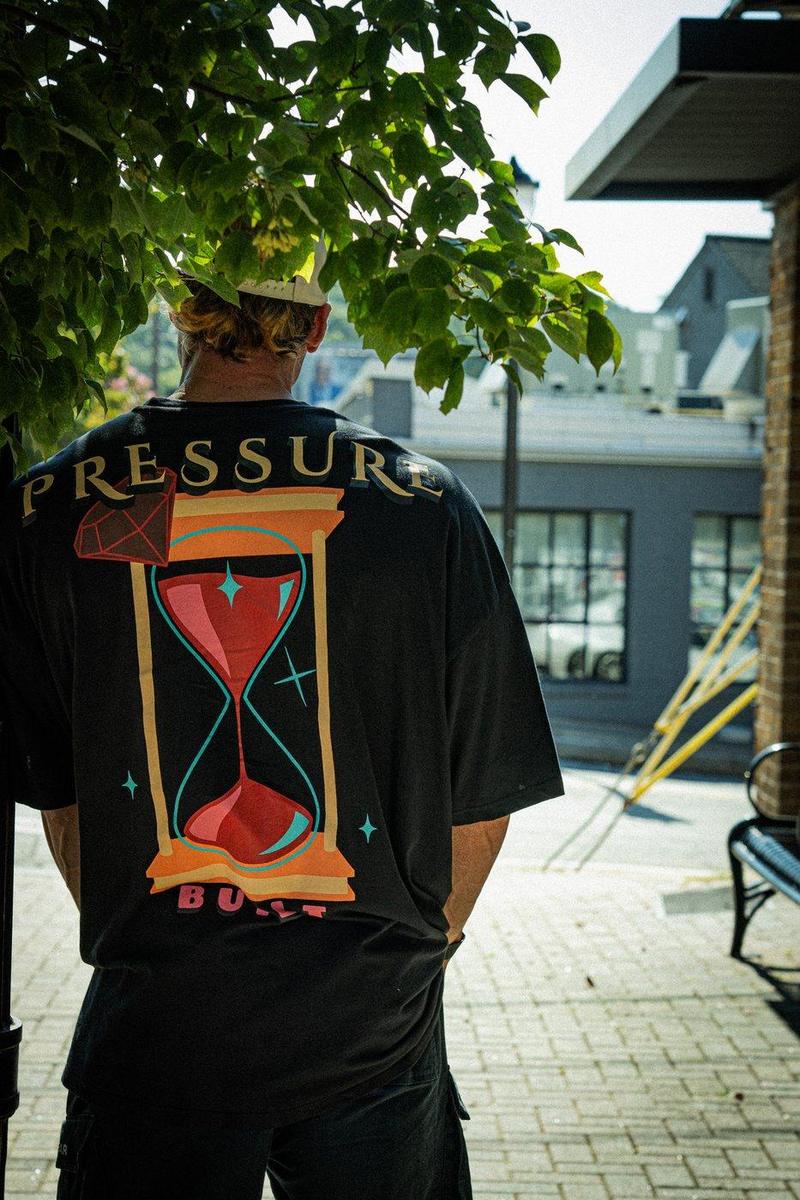 Athlete seen from behind in an ERND Pressure hourglass tee under a tree on a city sidewalk