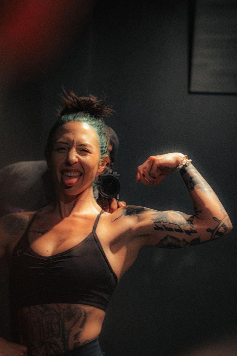 Tattooed athlete flexing and laughing at the camera in a gym mirror
