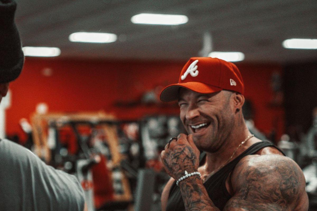 Bodybuilder in a red cap laughing between sets