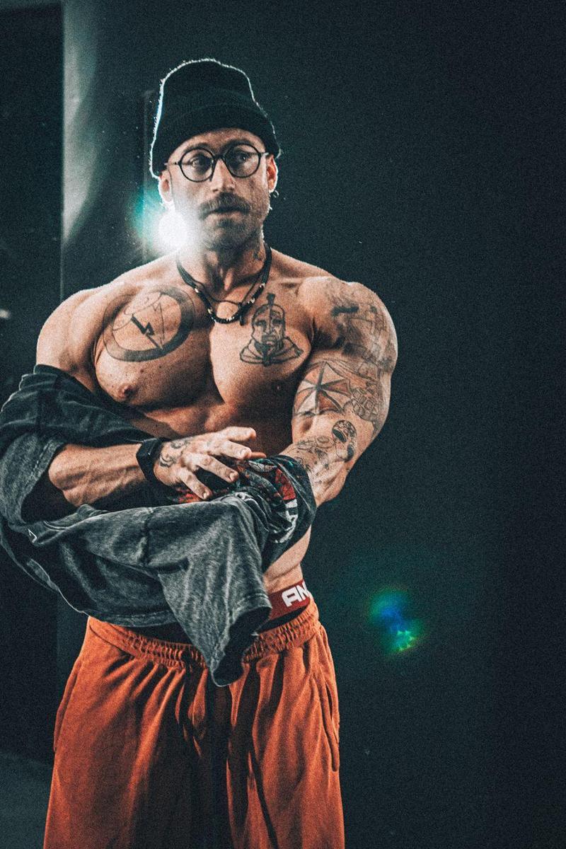 Tattooed bodybuilder pulling off his shirt, backlit with a lens flare