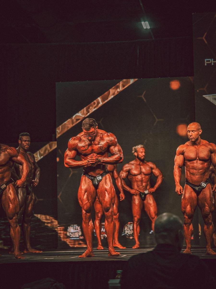Classic physique lineup on stage, the center competitor hitting a most muscular